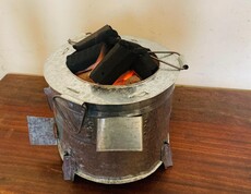 Energiesparofen mit Biokohlebriketts reduziert den Verbrauch herkömmlicher Brennstoffe  Metallofen mit glühenden Briketts auf einem Holztisch.