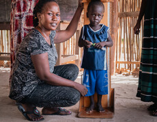 eine südsudanesische Frau misst die Größe eines Kleinkindes und blickt in die Kamera