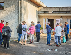 Menschen versammeln sich vor einem Gebäude in Böheimkirchen, um Hochwasser-Soforthilfe von Caritas zu erhalten. Ein Schild mit der Aufschrift "Caritas Wir helfen" ist sichtbar, während die Menschen in einer lockeren Gruppe stehen und miteinander sprechen.