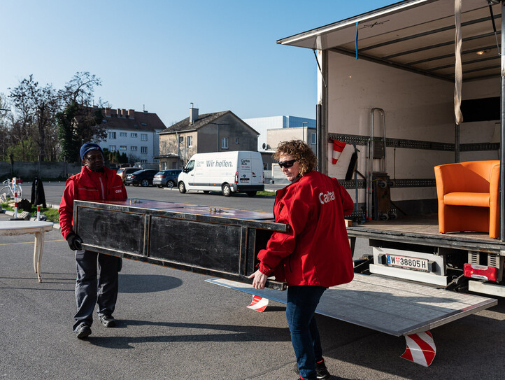 Das Bild zeigt Menschen beim Einladen eines Kastens in einen LKW