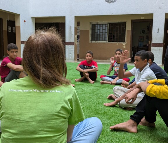 Das Straßenkinderzentrum geht auch auf die emotionalen Bedürfnisse der Kinder ein.  Eine Gruppe Kinder und eine Betreuerin sitzen auf einem Fußballrasen