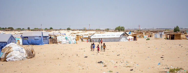 Flüchtlingscamp mit Zelten - ein paar Menschen sind in der Ferne zu sehen. 