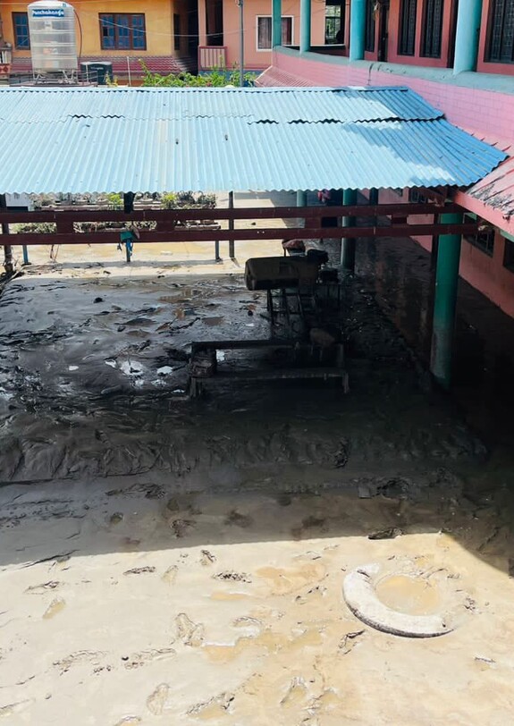 Schlamm und Wasser bedecken den Innenhof und einen überdachten Bereich eines Gebäudekomplexes in Nepal.