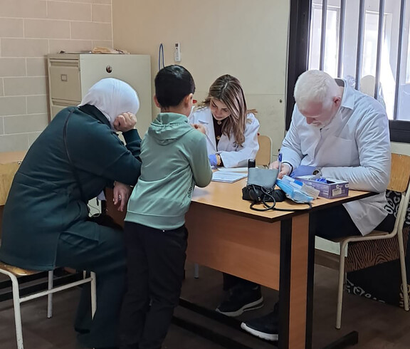 Eine Arztpraxis: Am Tisch sitzen zwei Patient*innen und medizinisches Personal.