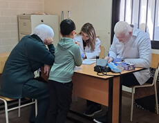 Eine Arztpraxis: Am Tisch sitzen zwei Patient*innen und medizinisches Personal.