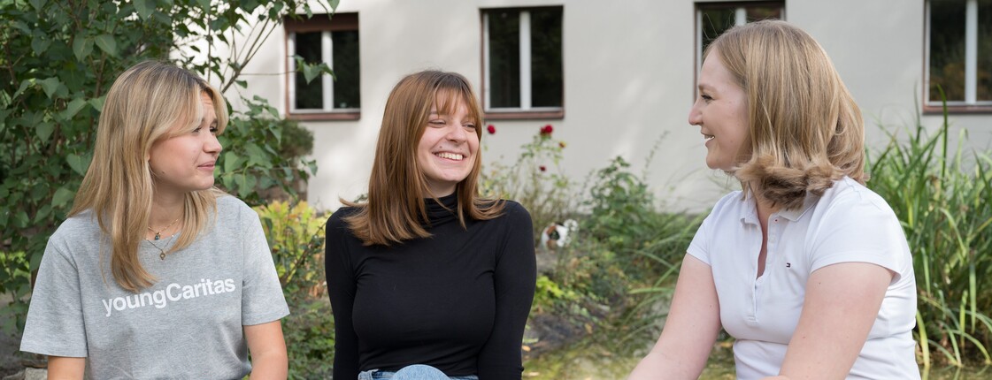 Drei Frauen sitzen in einem Garten und unterhalten sich.