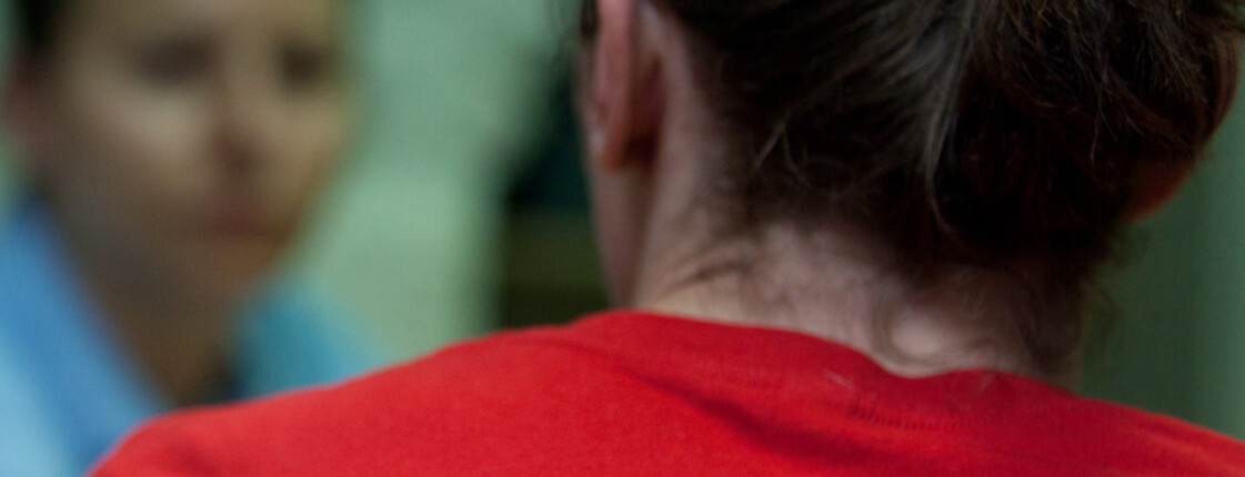 Eine Caritas-Mitarbeiterin im roten T-Shirt ist im Gespräch mit einer hilfesuchenden Person – stellvertretend für Beratung und Hilfe in schwierigen Situationen.