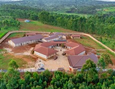  Drohnenaufnahme des vollständigen Gebäudekomplexes des Institut Supérieur de Nutrition et Paramédical de Simba inmitten grüner Hügel und Waldlandschaft; mehrere Backsteingebäude mit roten Dächern und Solarpanelen sind um einen zentralen Innenhof gruppiert, umgeben von einer Umfassungsmauer und terrassierten Feldern.