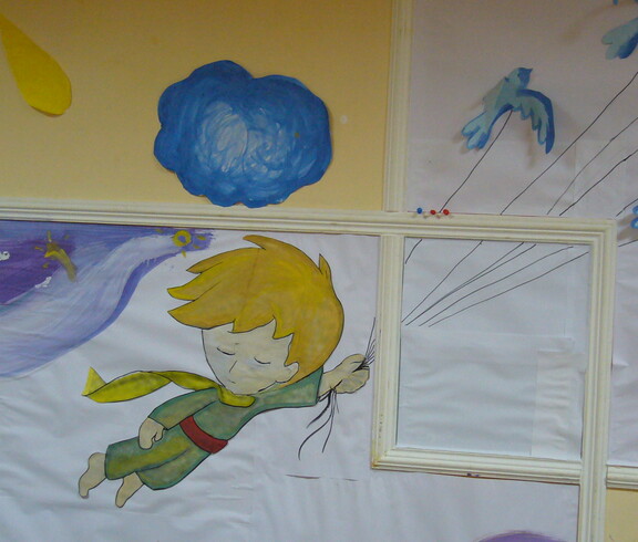 An einer gelben Wand hängen bemalte Papierblätter, die ein Gesamtbild ergeben, das den Kleinen Prinzen zeigt.