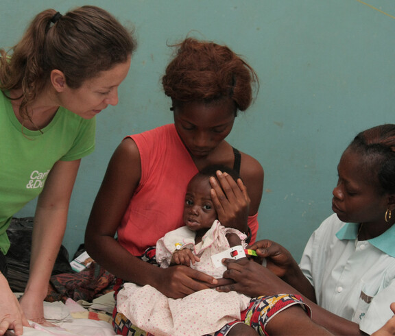 Eine Mutter hält ihr unterernährtes Baby, während eine Krankenschwester den Armumfang des Kindes misst
