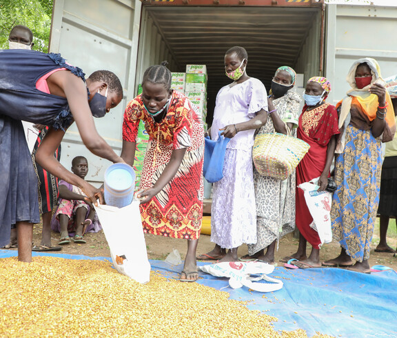 Gruppe von Frauen verschiedenen Alters steht vor einem Lieferwagen, zwei Frauen im Vordergrund portionieren Salz in einen Eimer bei einer Lebensmittelverteilung in Südsudan.