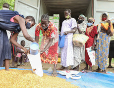 Gruppe von Frauen verschiedenen Alters steht vor einem Lieferwagen, zwei Frauen im Vordergrund portionieren Salz in einen Eimer bei einer Lebensmittelverteilung in Südsudan.