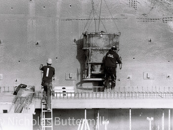 Zwei Bauarbeiter*in arbeiten an Betonwand mit Kran und Schalungselementen