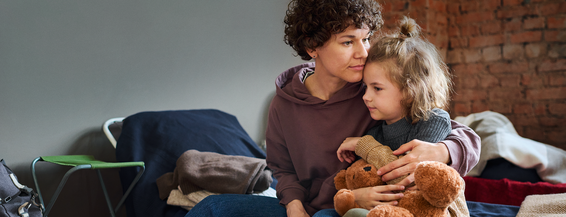 Alleinerziehende sind besonders häufig von Armut betroffen Eine Frau sitzt auf einer Bank, auf ihrem Schoß ein kleines Kind mit Kuscheltier in der Hand.