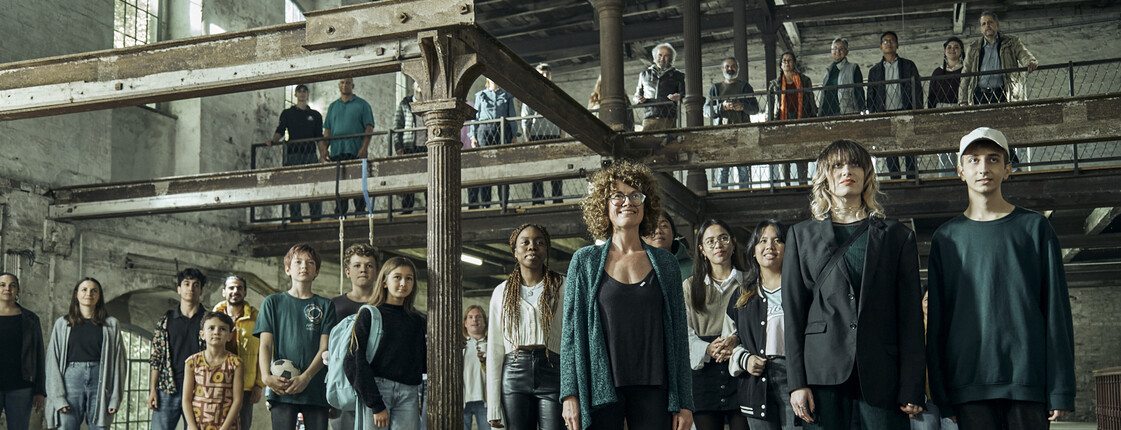 Eine Gruppe von Menschen steht in einem alten Fabrikgebäude alle blicken in die Kamera