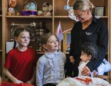 Kinder stehen vor einem Regal mit Spielsachen. Ein Kind umarmt eine Betreuerin, die die Kinder freundlich anlächelt.
