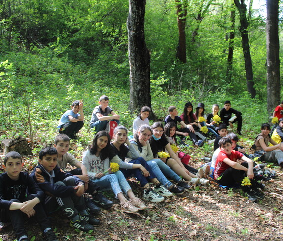 Eine große Gruppe Schüler*innen sitzt während eines Outdoor-Workshops neben einem Waldweg.