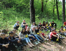 Eine große Gruppe Schüler*innen sitzt während eines Outdoor-Workshops neben einem Waldweg.