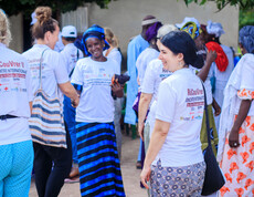 Mehrere Menschen stehen beisammen und unterhalten sich; viele tragen weiße T-Shirts mit Projektaufdruck.