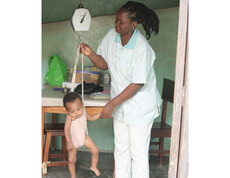 Eine Krankenschwester wiegt ein kleines Kind mit einer Hängewaage zur wöchentlichen Gewichtskontrolle nach stationärer Behandlung