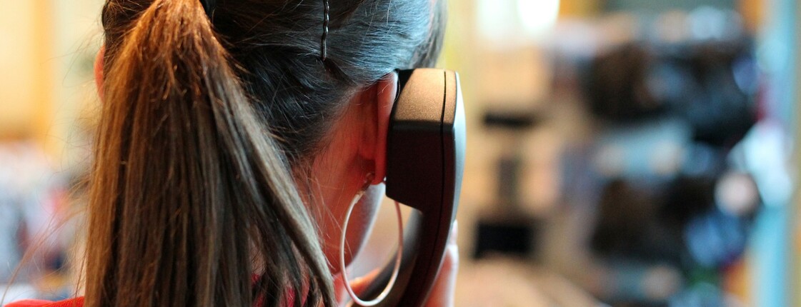Frau mit Kopfhörer-Headset von hinten fotografiert, im Hintergrund unscharf ein Büroraum