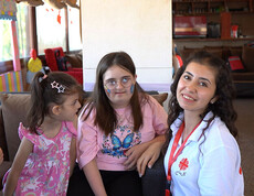 Betreuerin sitzt mit mehreren Kindern in einem Raum, einige Kinder haben sichtbare Beeinträchtigungen