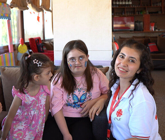 Betreuerin sitzt mit mehreren Kindern in einem Raum, einige Kinder haben sichtbare Beeinträchtigungen