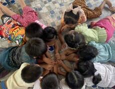 Mehrere Kinder liegen im Kreis auf dem Boden und halten ihre Hände in der Mitte zusammen.