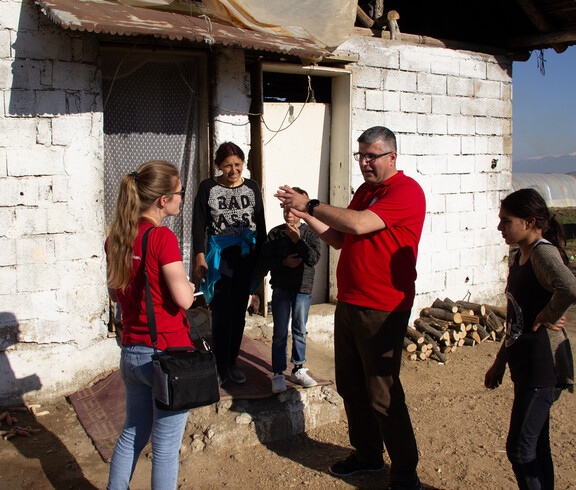 Caritas-Projektreferentin Theresa Sacher steht mit einem Jungen und mehreren Erwachsenen vor einem Haus. Ein Mann in rotem Shirt, der Leiter des Lernzentrums, gestikuliert beim Sprechen. Die Gruppe unterhält sich im Freien.
