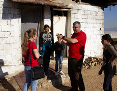 Caritas-Projektreferentin Theresa Sacher steht mit einem Jungen und mehreren Erwachsenen vor einem Haus. Ein Mann in rotem Shirt, der Leiter des Lernzentrums, gestikuliert beim Sprechen. Die Gruppe unterhält sich im Freien.
