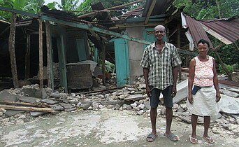 Ein Mann und eine Frau stehen vor einem zerstörten Haus