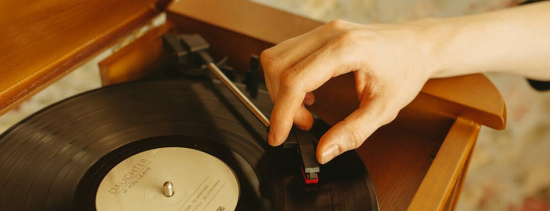 Hand legt Nadel auf Schallplatte  Hand legt Tonarm auf schwarze Vinylplatte mit Oldies der 60er bis 80er in Holzplattenspieler