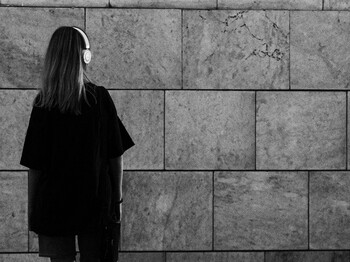 Jugendliche Person mit Kopfhörern steht allein vor einer Steinwand, Sinnbild für Rückzug und Einsamkeit im Jugendalter.