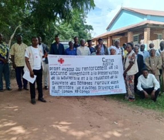 Gruppe von Frauen und Männern steht im Freien vor einem Gebäude und hält gemeinsam ein Banner.