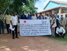 Gruppe von Frauen und Männern steht im Freien vor einem Gebäude und hält gemeinsam ein Banner.
