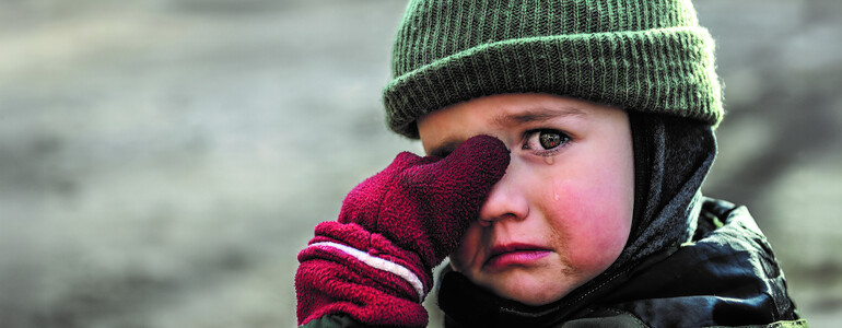Kind mit Mütze und roten Handschuhen wischt sich weinend die Augen ab
