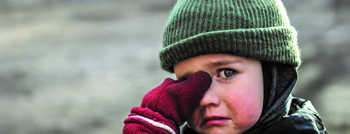Kind mit Mütze und roten Handschuhen wischt sich weinend die Augen ab
