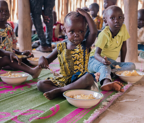 Südsudanesische Kinder sitzen am Boden und essen