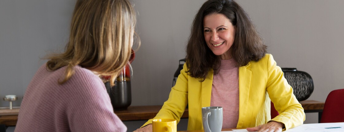 Zwei Frauen sitzen sich gegenüber und besprechen Dokumente, die vor ihnen auf dem Tisch liegen.