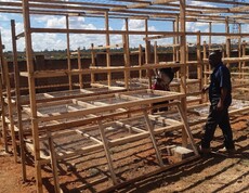 Ein wichtiger Beitrag zur nachhaltigen Energieversorgung in Lubumbashi  Mehrere Personen arbeiten an einer großen Holzkonstruktion mit Trockengestellen im Freien.