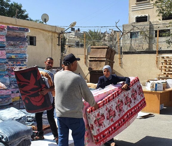 Helfer*innen übergeben Matratzen an Betroffene in einem offenen Hof in Gaza.