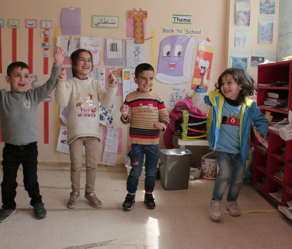 Sechs Kinder machen eine koordinierte Gruppenübung in einem bunt dekorierten Klassenraum im Libanon