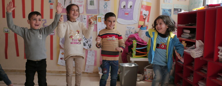 Sechs Kinder machen eine koordinierte Gruppenübung in einem bunt dekorierten Klassenraum im Libanon