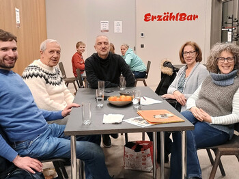 Interkultureller Treff im Integrationshaus Fünf Personen sitzen in einem Neubau an einem Tisch und schauen in die Kamera.