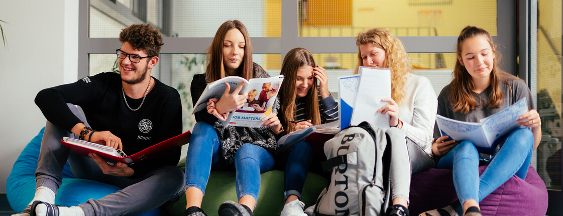 Ein Schüler und fünf Schüler*innen sitzen auf Sitzsäcken im Gand der Schule und lernen miteinander.