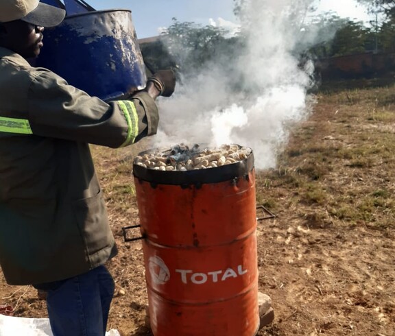 Im Projekt PERDURER werden Maiskolben karbonisiert, um Biokohle herzustellen  Ein Mann befüllt einen Metallofen mit Maiskolben, aus dem Rauch aufsteigt.
