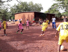 Kinder spielen Fußball in einem Ferienlager auf einem Sandplatz.