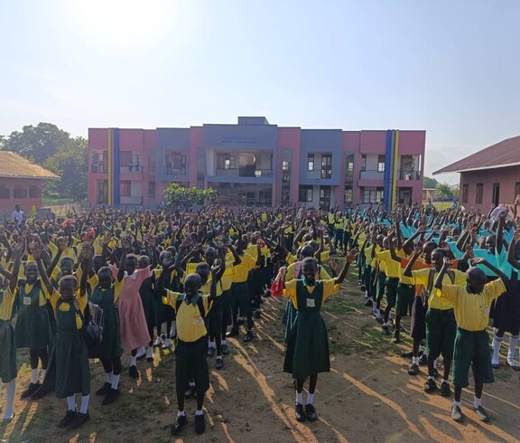 Schüler*innen stehen in Schuluniform aufgereiht vor dem Neubau und haben die Arme in der Luft.