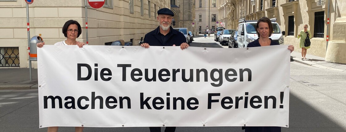 Drei Menschen halten ein Plakat mit der Aufschrift "Die Teuerungen machen keine Ferien!"