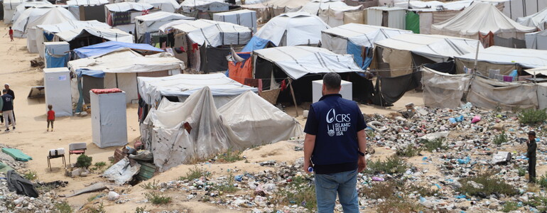 Eine Person mit Caritas-Weste blickt auf ein dichtes Zeltlager im Krisengebiet Gaza.